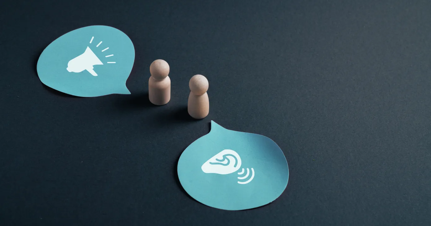 Active listening concept with wooden figures and speech bubbles showing speaking and attentive ear communication