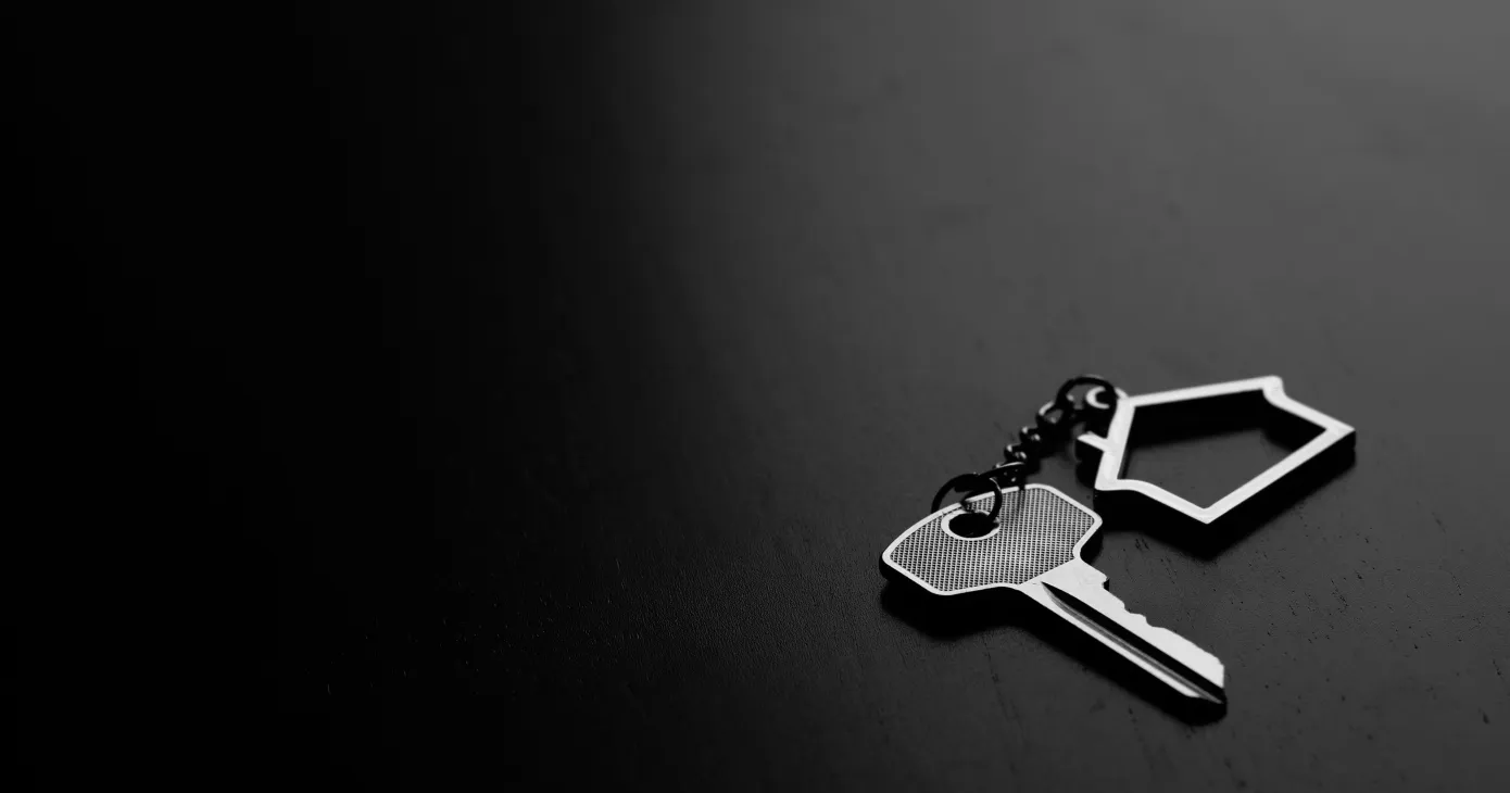 Home key with house keyring on black wood table in dark tone, real estate concept
