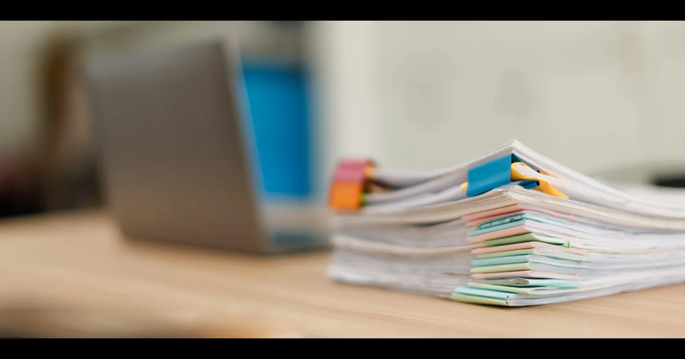 Pile de documents annotés d'onglets de couleur devant un ordinateur portable