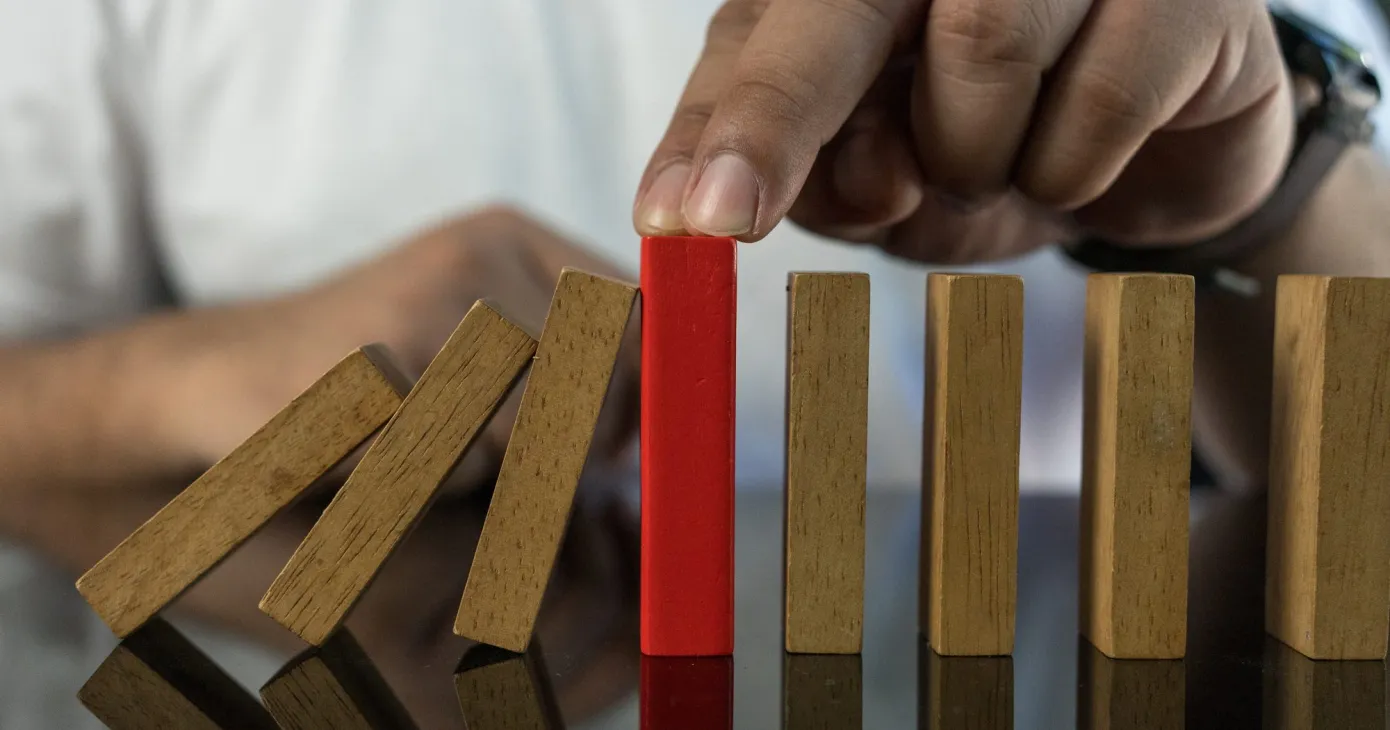 Main interrompant la chute d'une rangée de dominos en bois