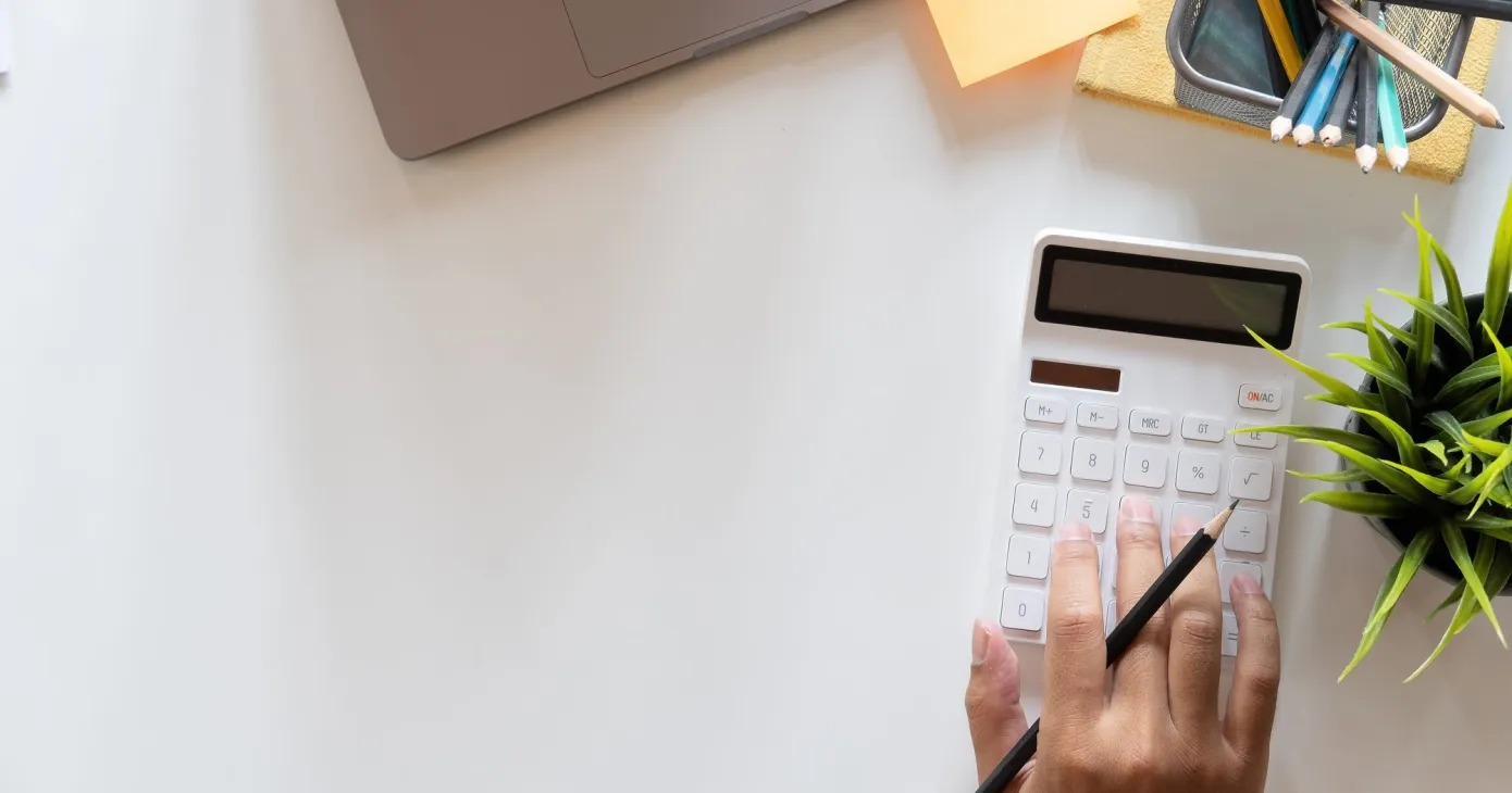 Main utilisant une calculatrice à côté d'un ordinateur portable, vue de dessus