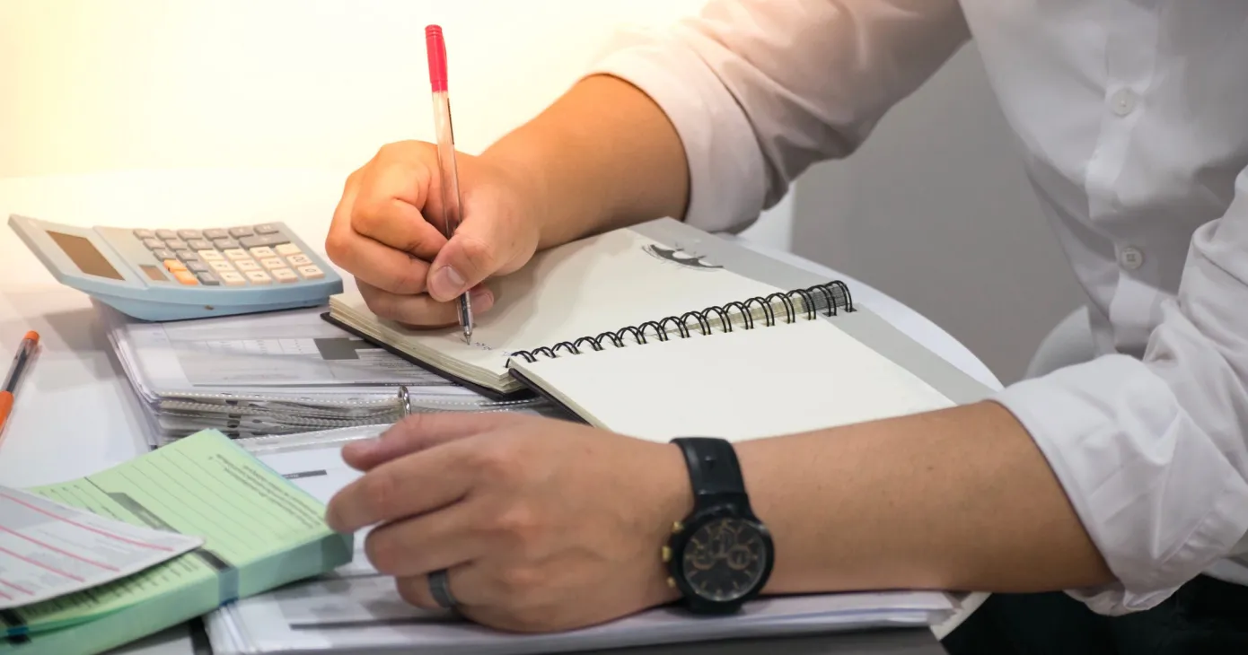 Personne prenant des notes dans un carnet à côté de dossiers empilés