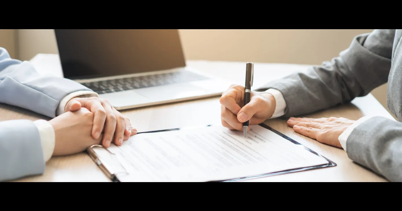 Deux personnes autour d'une table, l'une signant un document